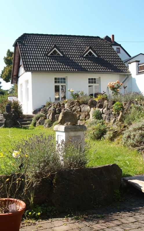 Ferienwohnung Zauberhaft Fam. Münch in Schalkenmehren - Außenansicht mit grüner Wiese, Blumen und Aufgang zur Terrasse